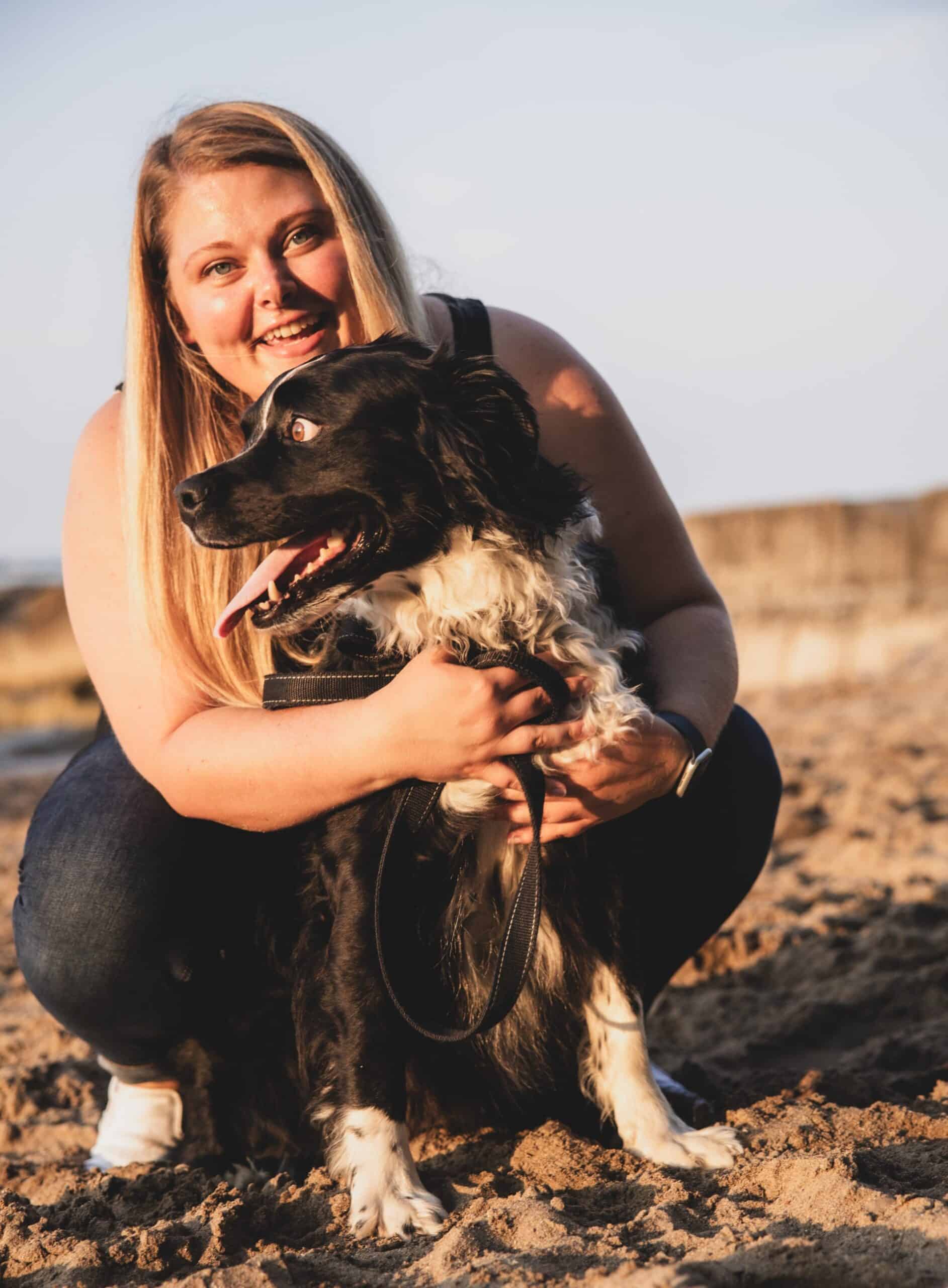 blond woman on the beach holding black and white fluffy dog